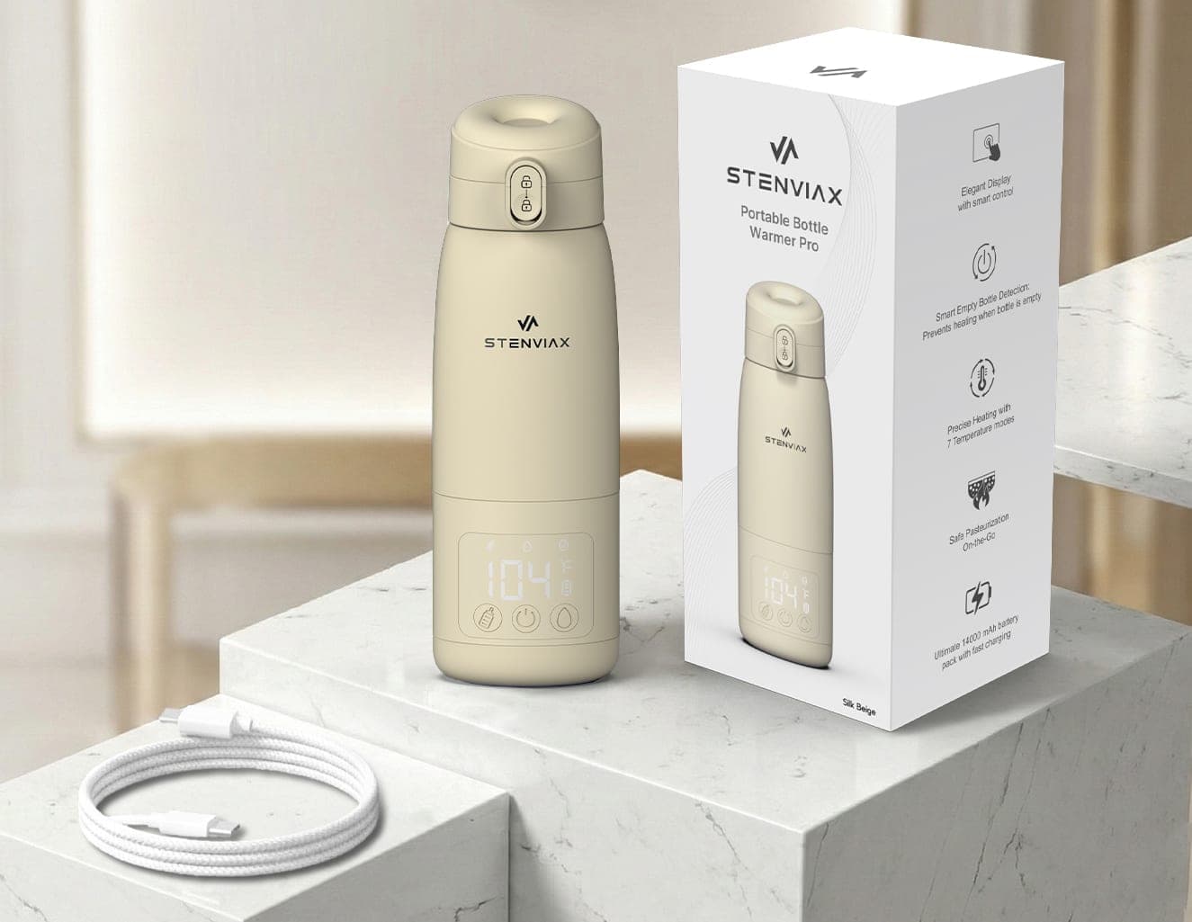 The Silk Beige warmer standing on a white marble plinth beside its retail carton, a braided USB-C charging cable coiled on the step below