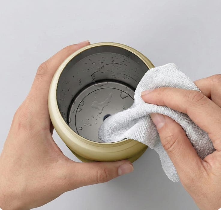 Two hands drying the inside of the Silk Beige warmer's steel chamber with a cloth