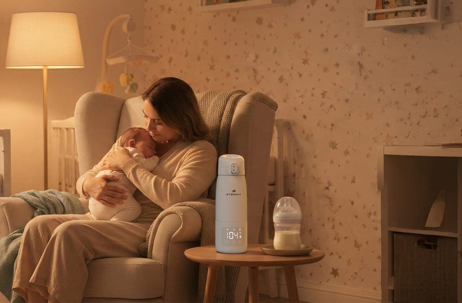 A mother holding her newborn in a lamplit nursery armchair, with the Stenviax warmer and a bottle on the side table