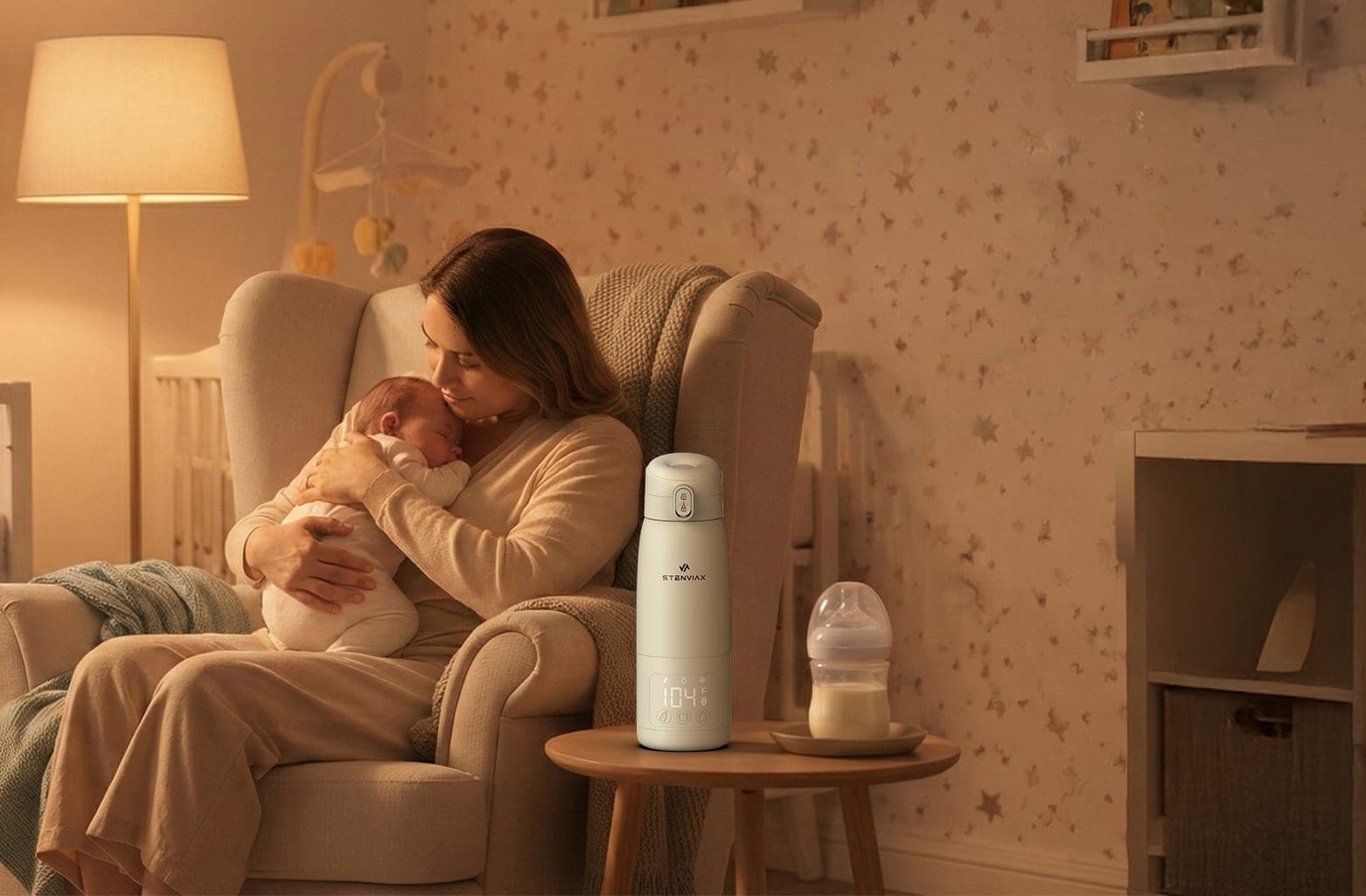 A mother cradling her sleeping newborn in a nursery armchair by lamplight, the Silk Beige warmer and a bottle of milk on the side table beside her